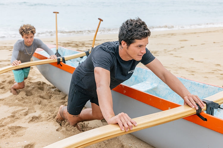 Micah DeSoto pushing a canoe up the beach in his Xcel T-shirt