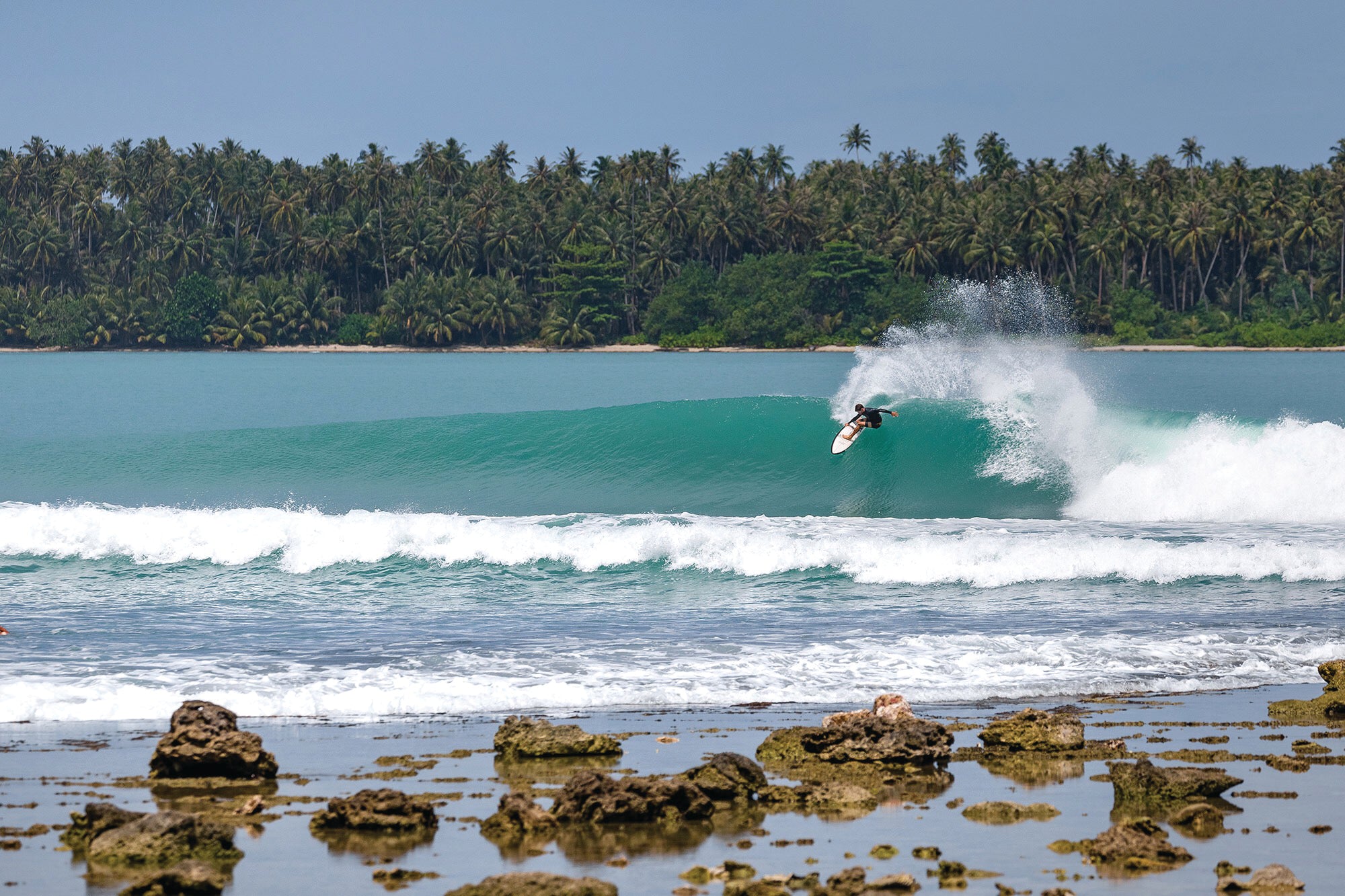 surfer on wave in front of rocky beach