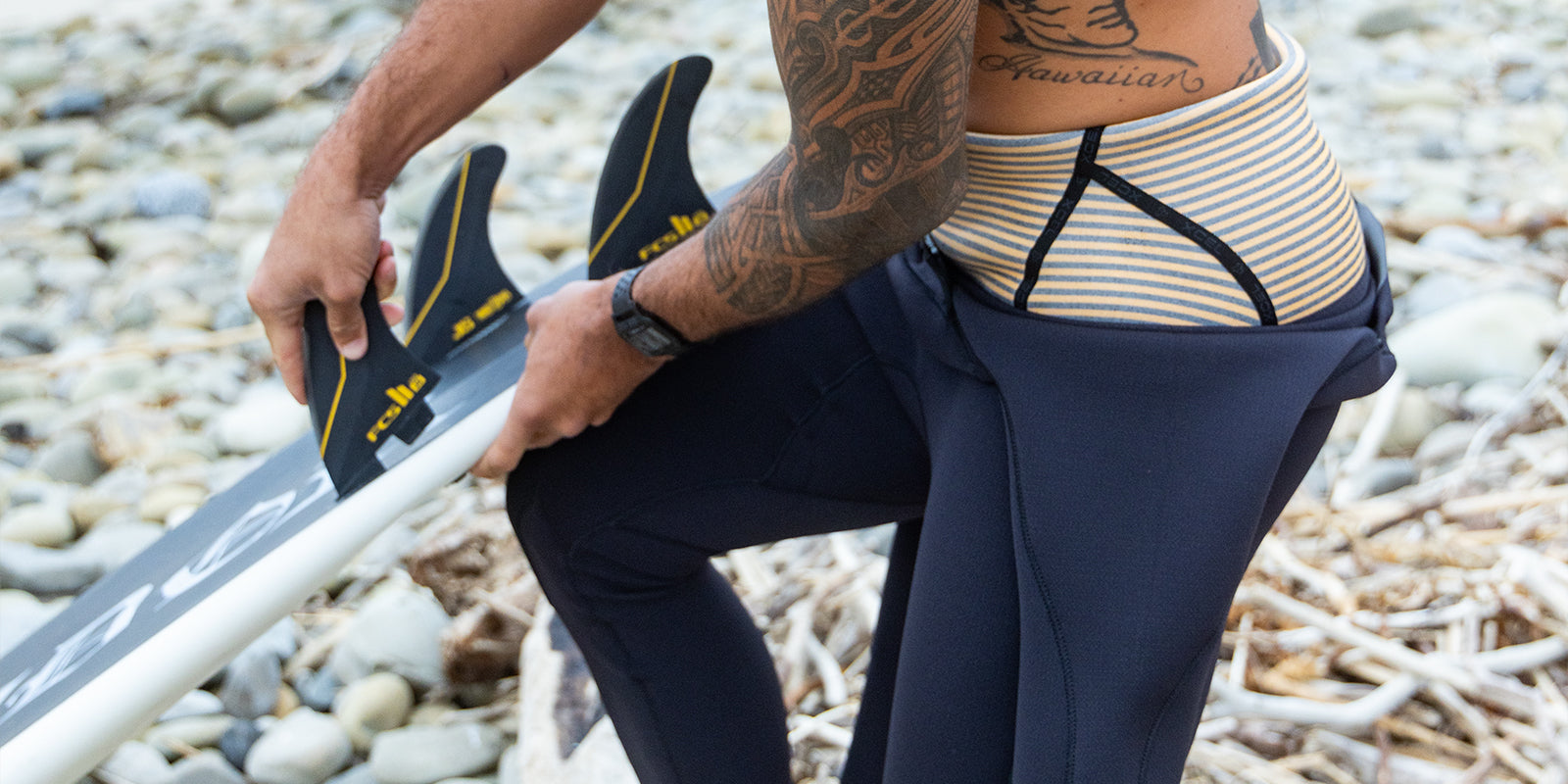Zeke Lau holding his surfboard on the beach while getting into his wetsuit