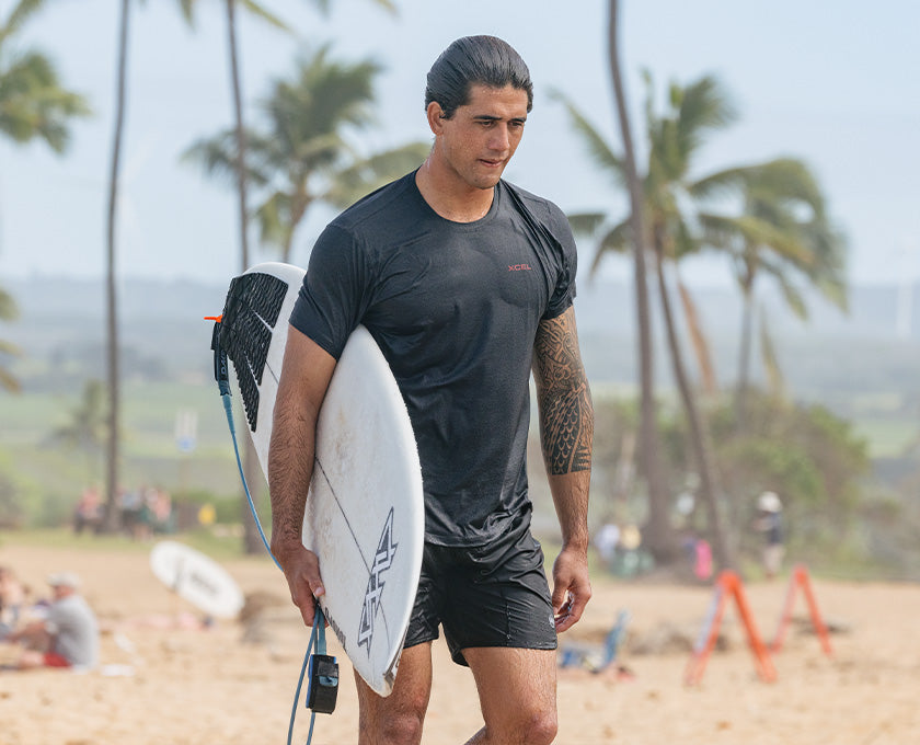 surfer wearing rash guard and holding surfboard on beach
