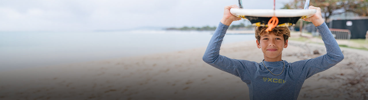 youth surfer on the beach with a surfboard over their head in Xcel UV shirt