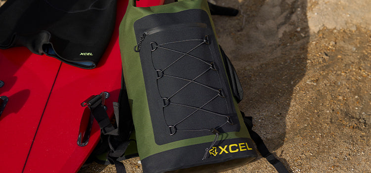 Xcel dry pack sitting on the beach next to a surfboard